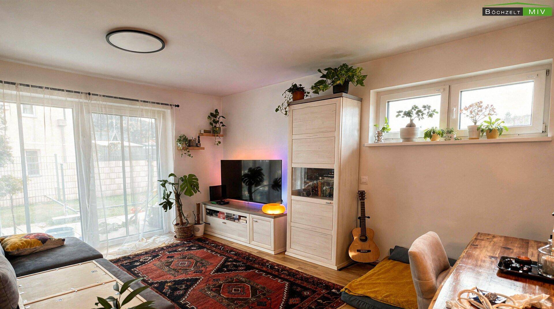 Helles Wohnzimmer mit Sofa, Fernseher und Zugang zum Garten oder zur Terrasse.