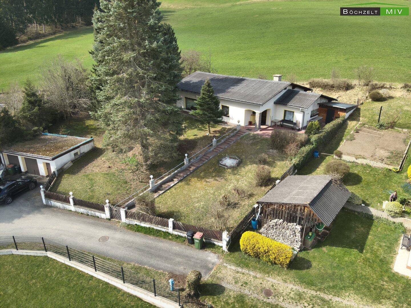 Luftaufnahme des Hauses mit Zufahrt, Doppelgarage und Holzschuppen, umgeben von gepflegten Grünflächen.