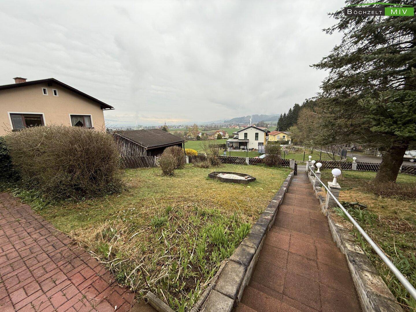 Gartenweg mit Ziegelpflaster und Treppe, die zum Haus führt, umgeben von Rasen und Sträuchern.
