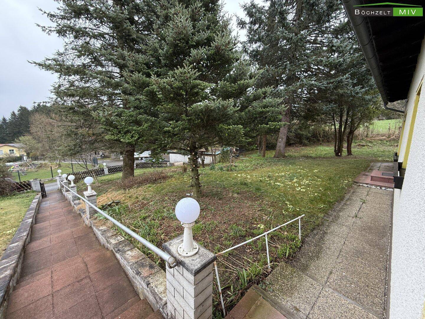 Treppenaufgang zum Haus, gesäumt von Laternen und Bäumen, mit Blick auf den weitläufigen Garten.