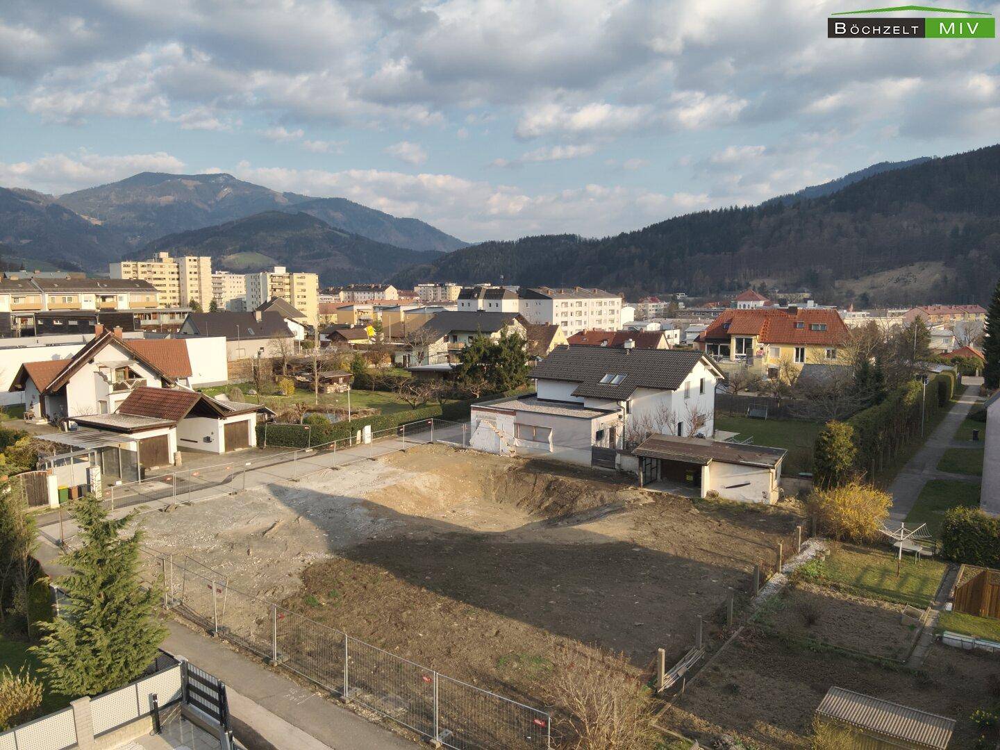 Aussicht auf das Baugrundstück und die umliegende Bebauung mit Bergkulisse und weitem Himmel.