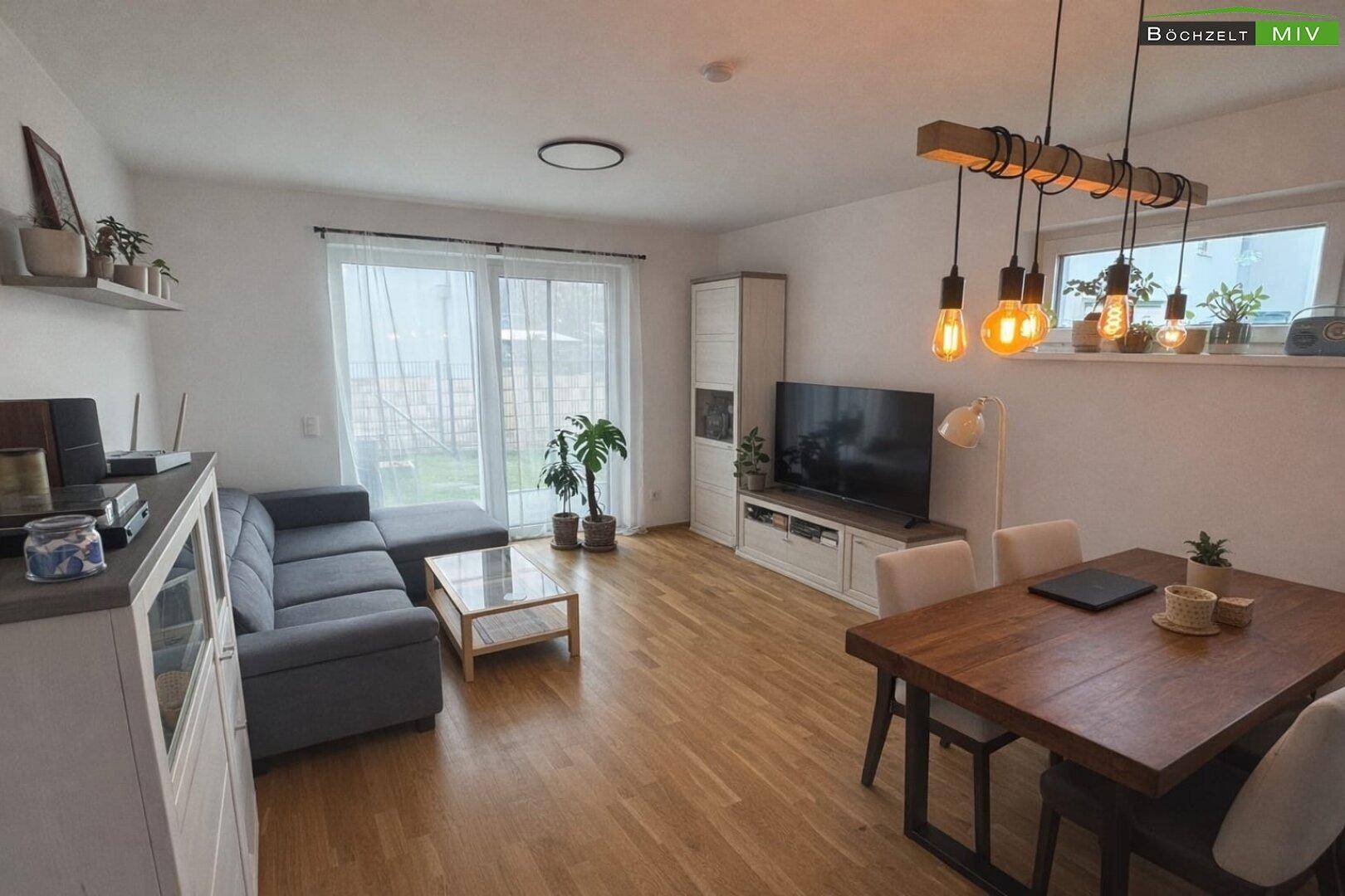 Moderner Wohn-Essbereich mit Holzboden, großen Fenstern und direktem Zugang zum Garten.