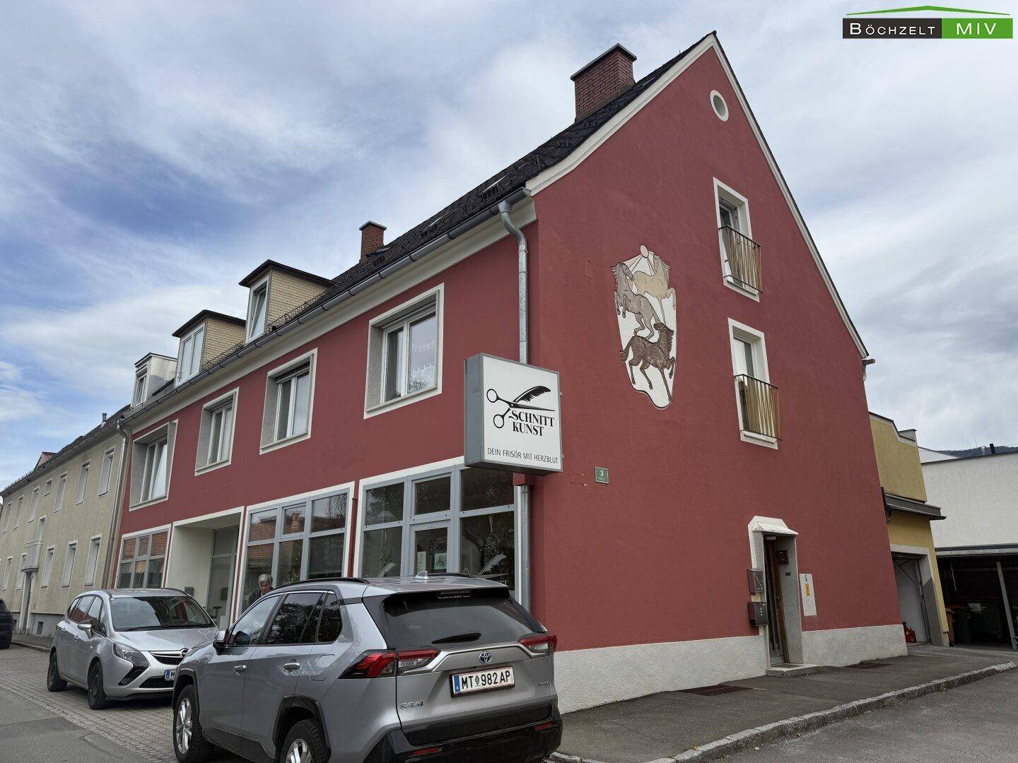 Detailansicht der roten Gebäudefassade mit Giebel, Fenstern und einem Schild an der Seite des Hauses.