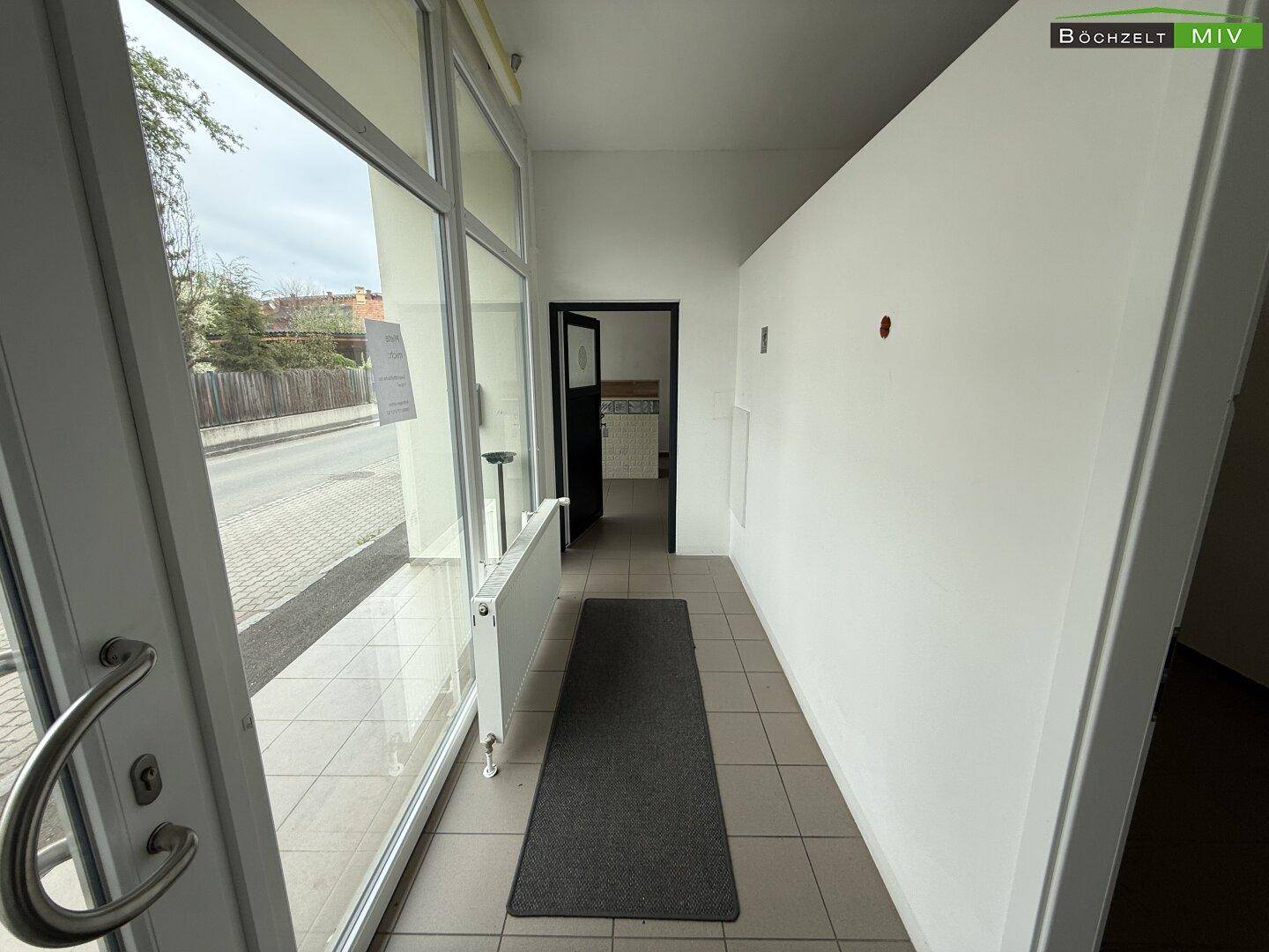 Heller Eingangsbereich mit Fliesenboden, großen Glasfenstern und Blick zur Straße.