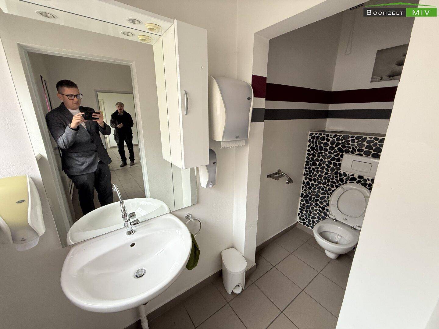 Toilettenraum mit Waschbecken, Spiegel und einer Wand mit dekorativen Kieselsteinfliesen.