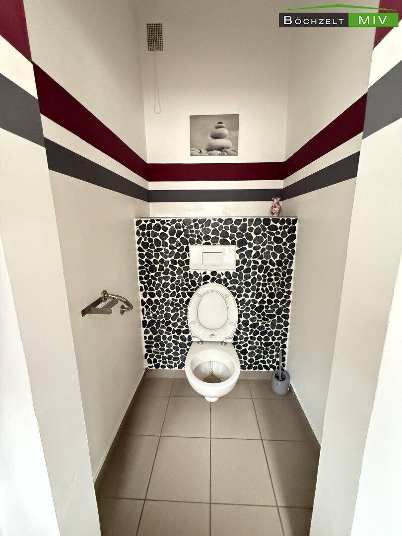 Toilettenbereich mit Wand-WC und einer dekorativen Wandgestaltung aus Kieselsteinfliesen.