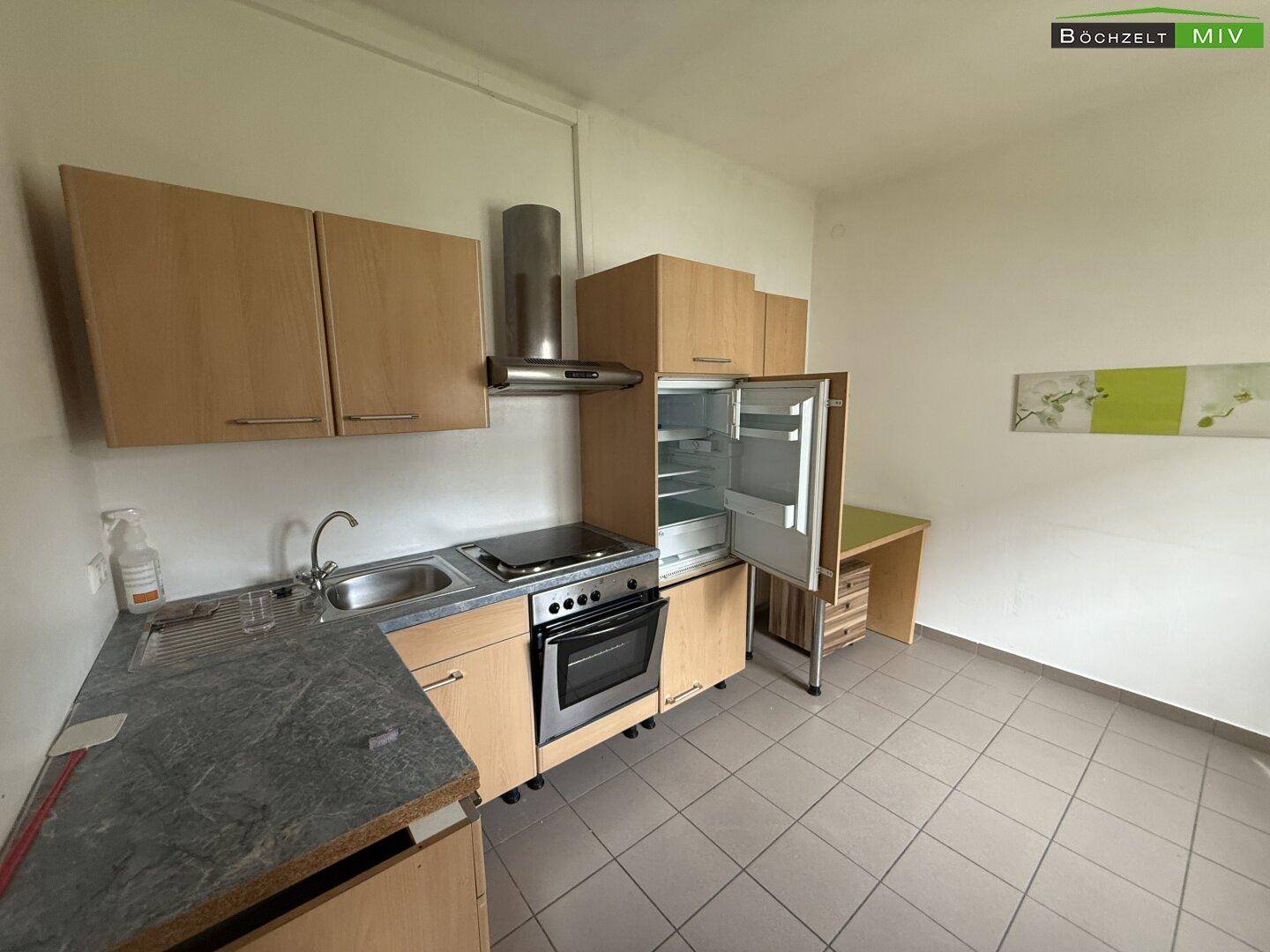 Kleine Küche mit Holzschränken, Spüle, Herd und Kühlschrank in einem hellen Raum.