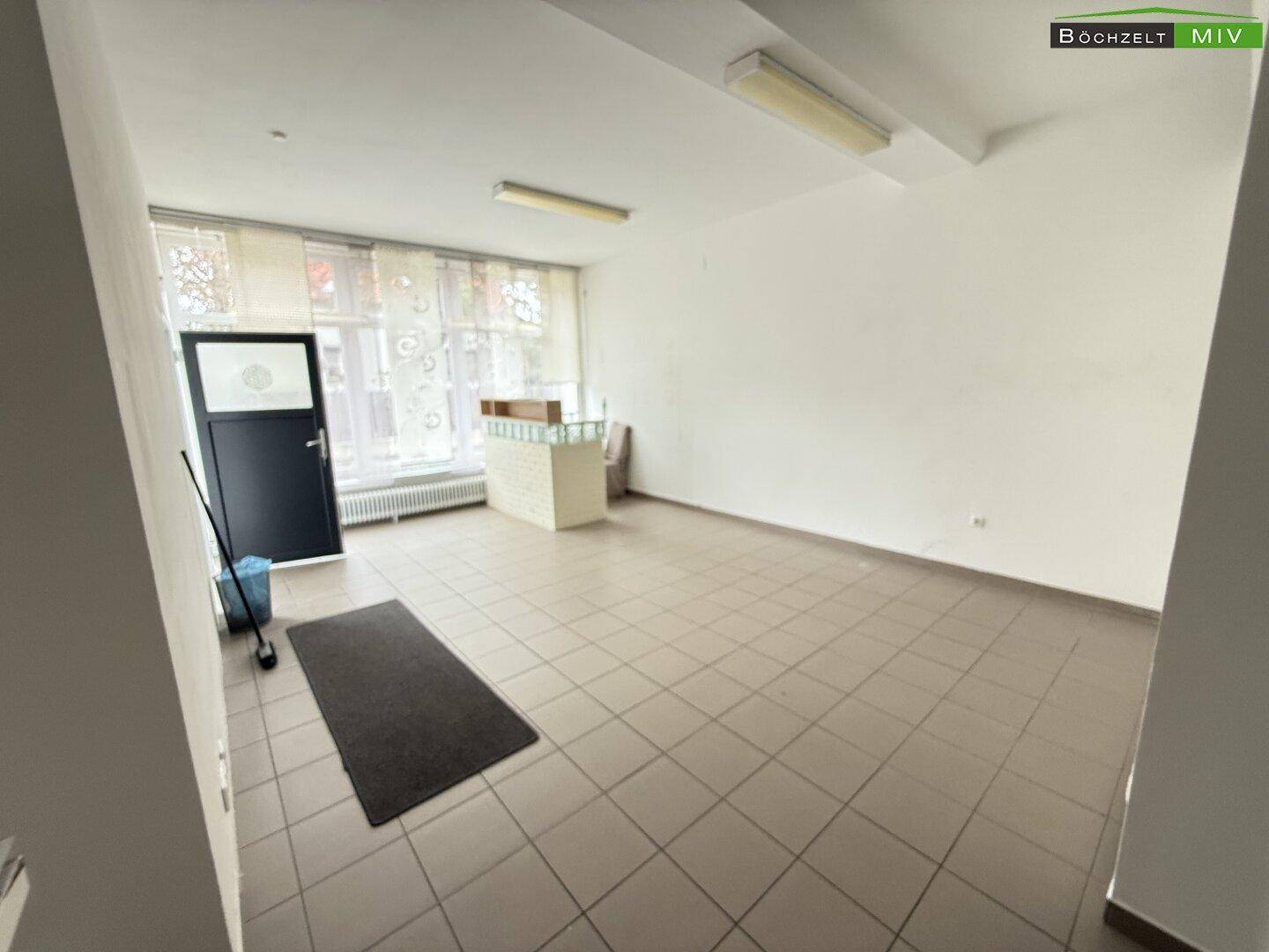 Großer, leerer Verkaufsraum mit Fliesenboden, großen Fenstern und einer Theke.