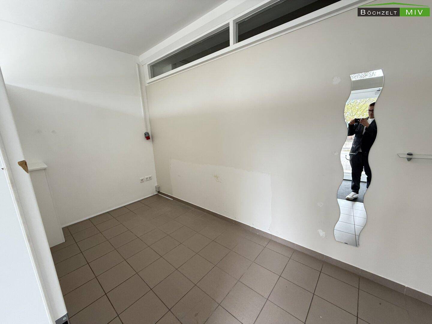 Leerer Raum mit Fliesenboden, weißen Wänden und einem dekorativen Spiegel an der Wand.