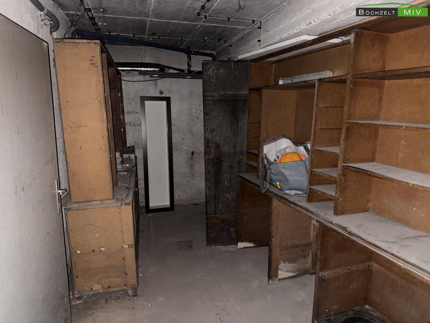 Kellerraum mit Regalen, unfertigen Wänden und sichtbaren Rohren an der Decke.