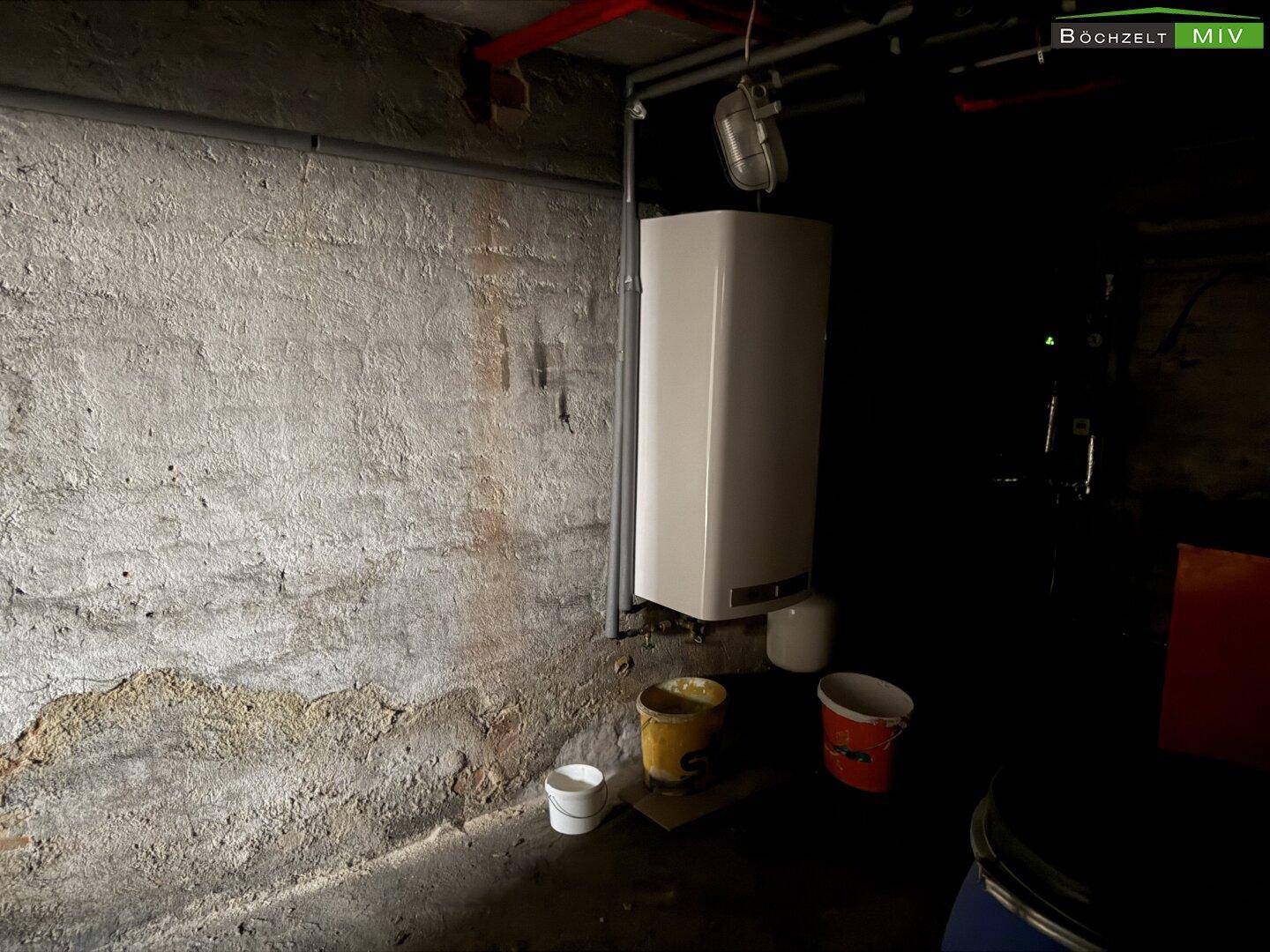 Kellerraum mit Boiler, rauen Wänden und Eimern auf dem Betonboden.
