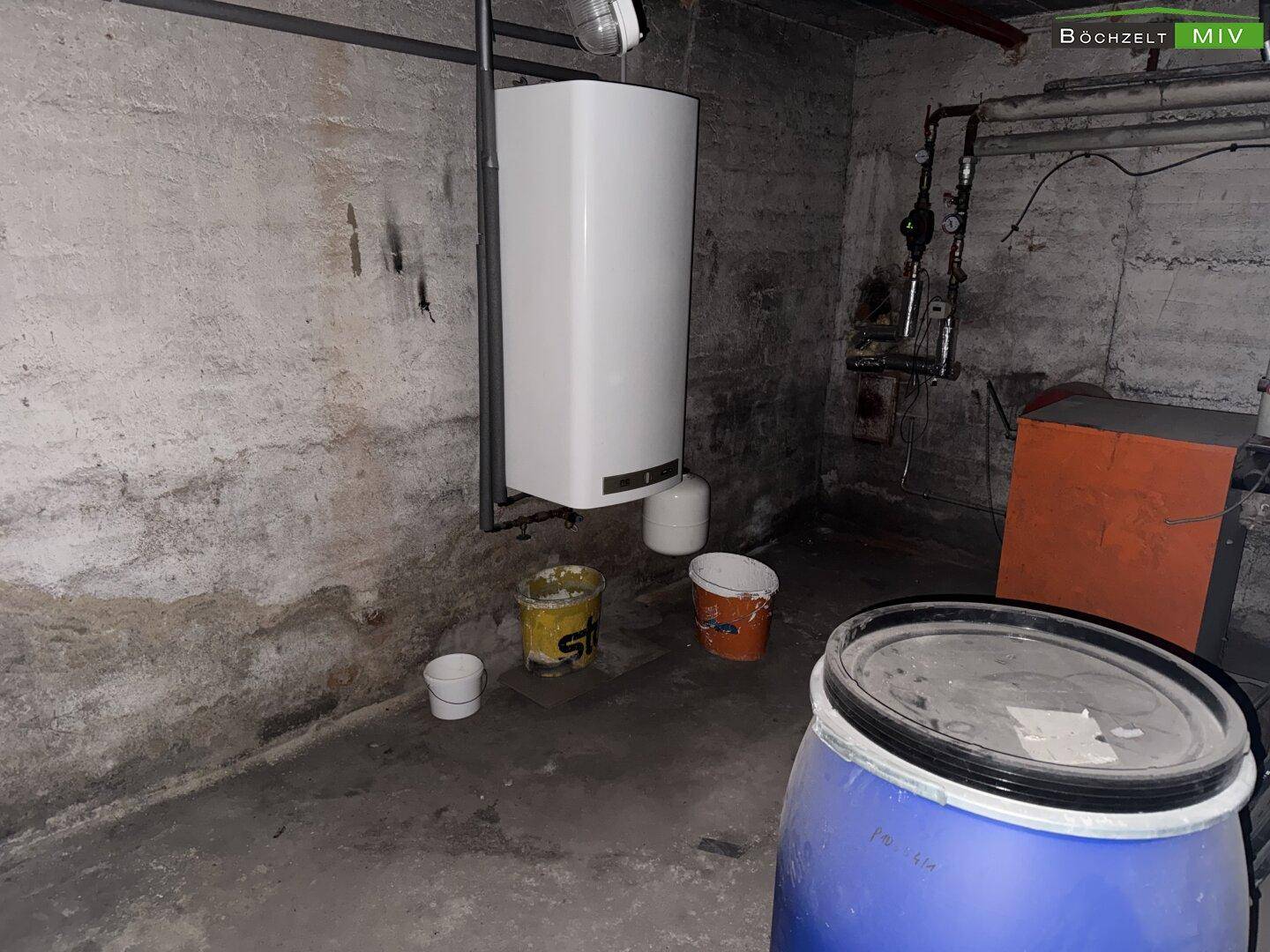 Dunkler Kellerraum mit Boiler, Rohren und einem großen blauen Fass.