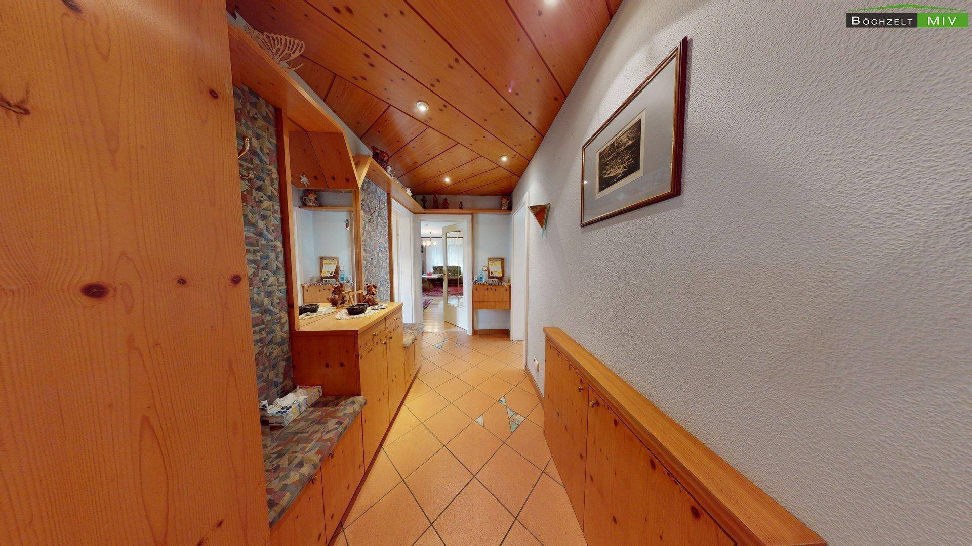 Langer Flur mit Holzpaneeldecke, Fliesenboden und eingebauten Holzschränken, die zu weiteren Räumen führen.