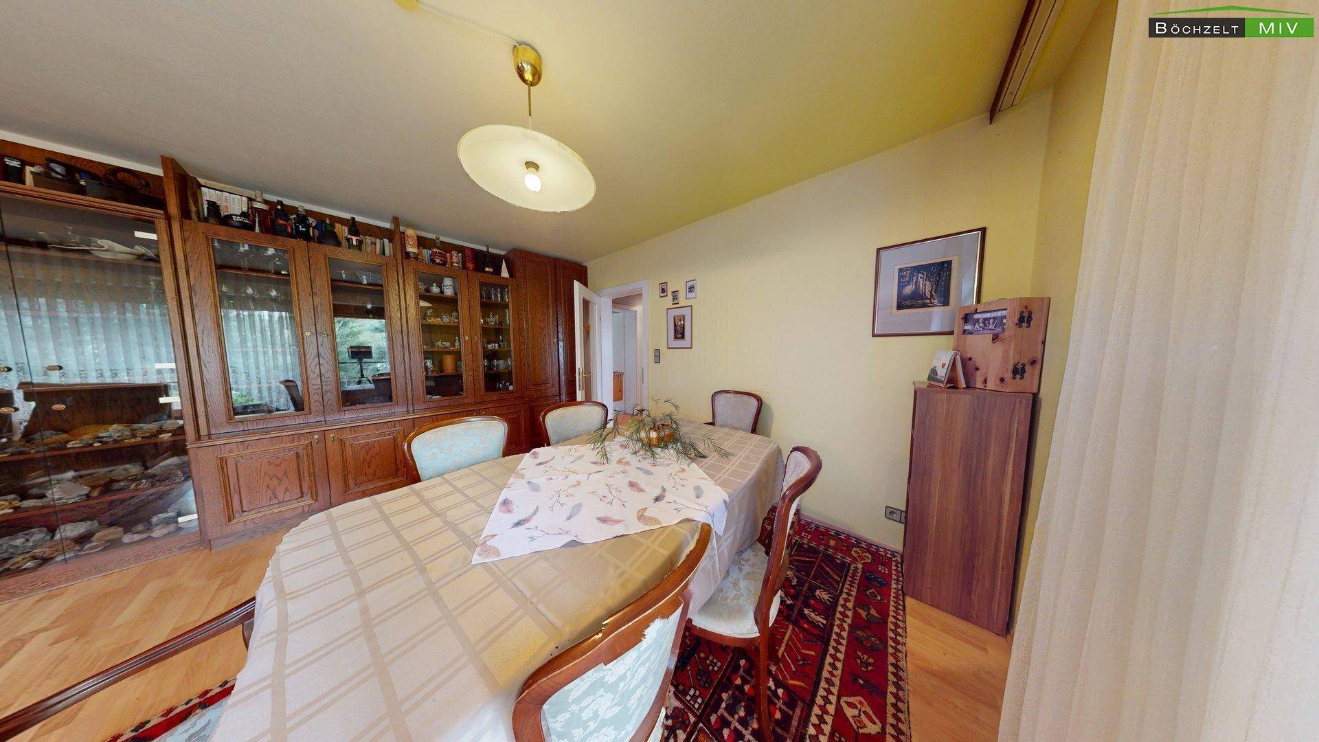 Eleganter Essbereich mit großem Holztisch, Vitrinenschrank und Parkettboden, verbunden mit dem Wohnzimmer.