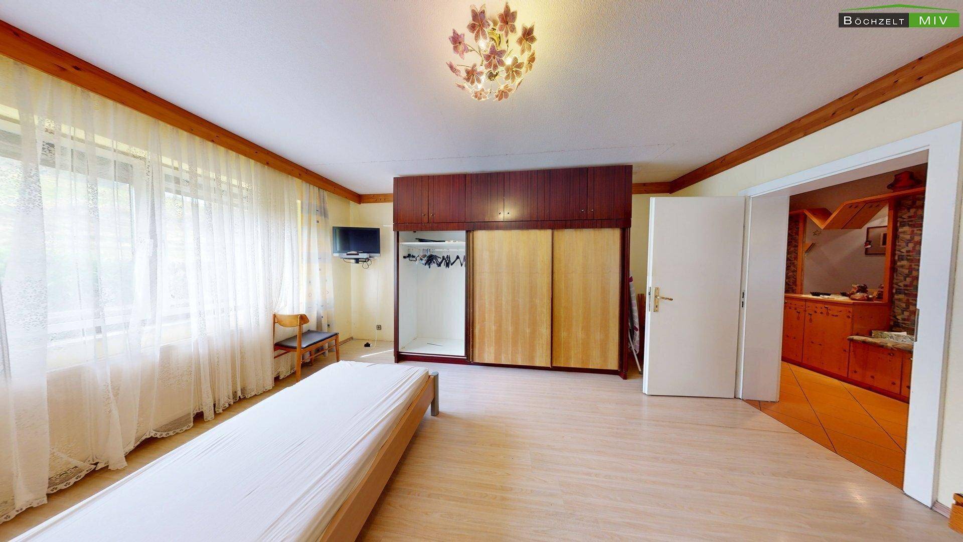 Helles Schlafzimmer mit Laminatboden, großem Schrank und Zugang zu einem weiteren Raum, gut beleuchtet.