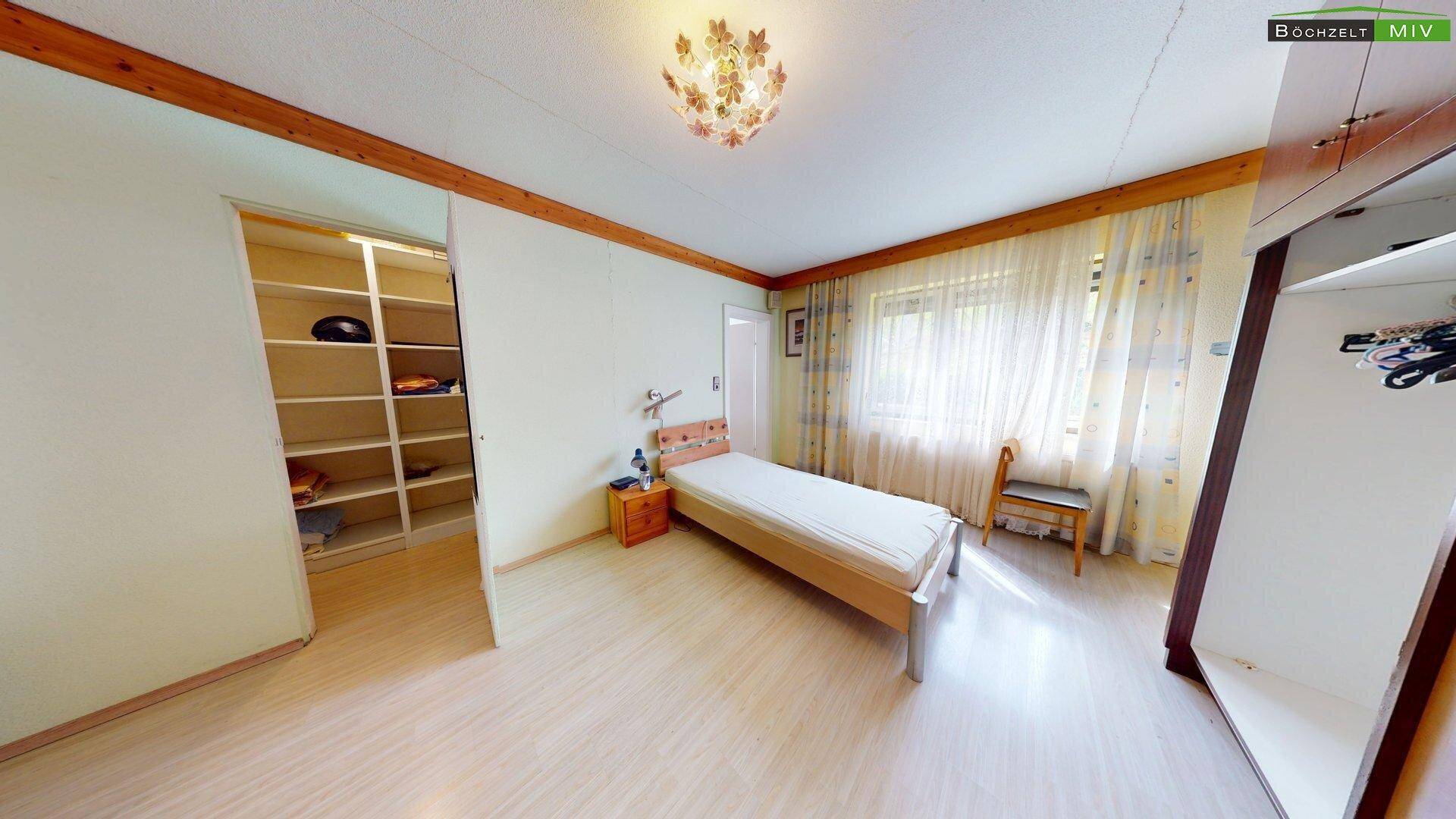 Schlafzimmer mit hellem Laminatboden, Einzelbett und offenem Kleiderschrank, der viel Stauraum bietet.
