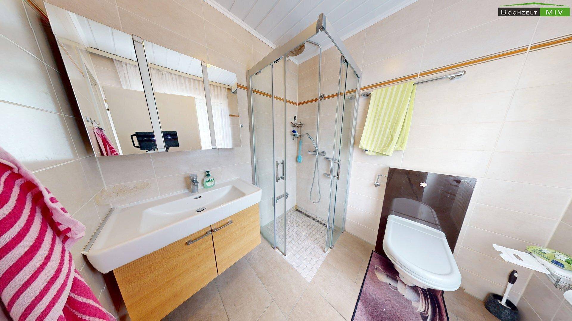 Modernisiertes Badezimmer mit Duschkabine, Waschbeckenunterschrank und Wand-WC, hell gefliest.