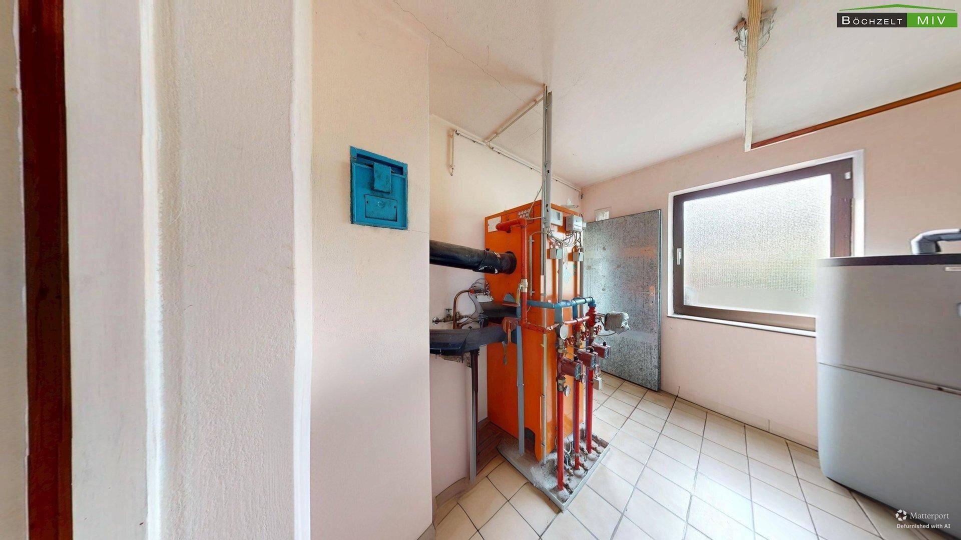 Heizraum mit großem Heizkessel und Rohrleitungen, ausgestattet mit einem Fenster für Belüftung.