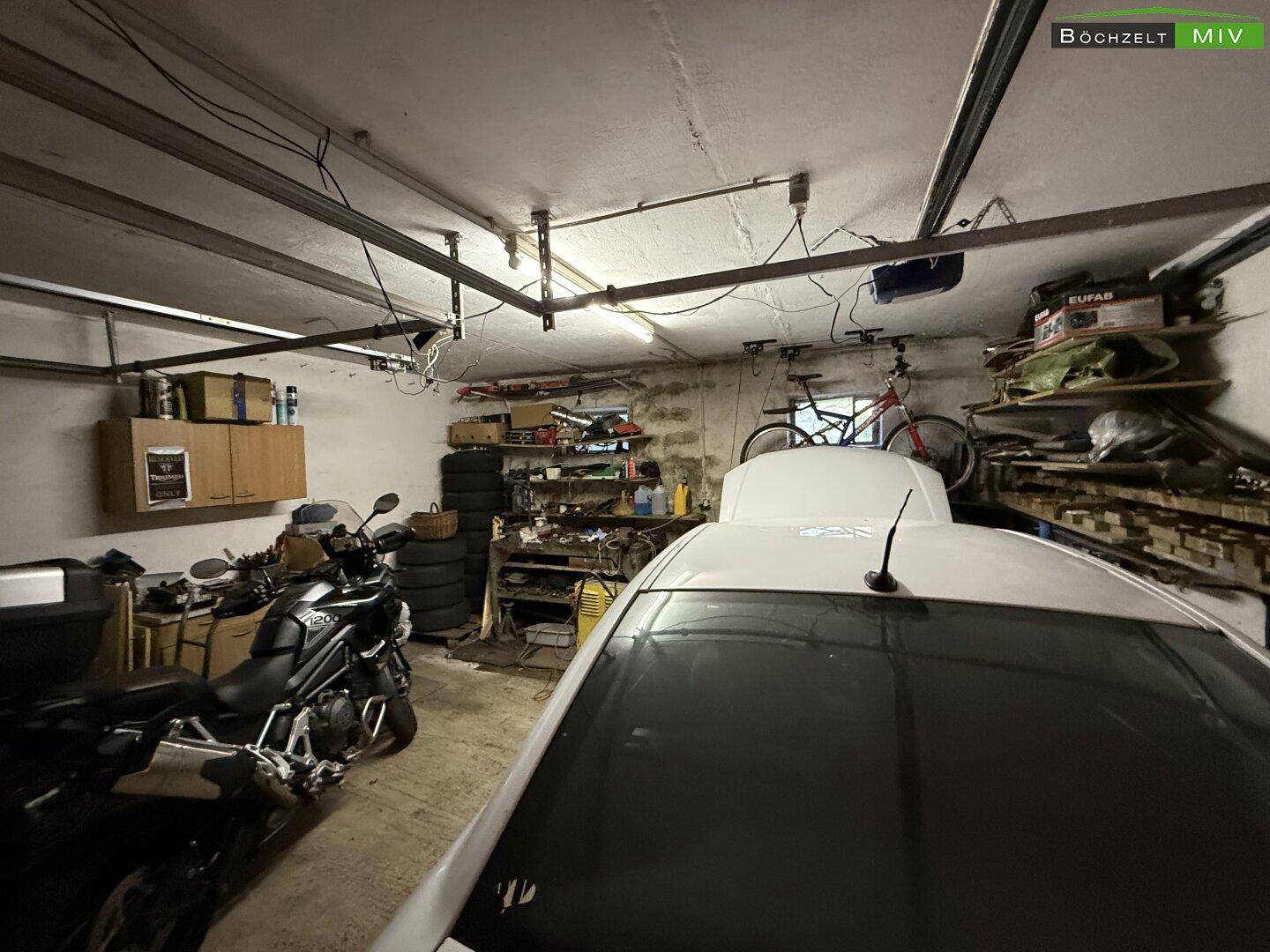 Innenansicht einer Garage mit Stauraum, Werkzeugen und geparktem Fahrzeug, gut beleuchtet.