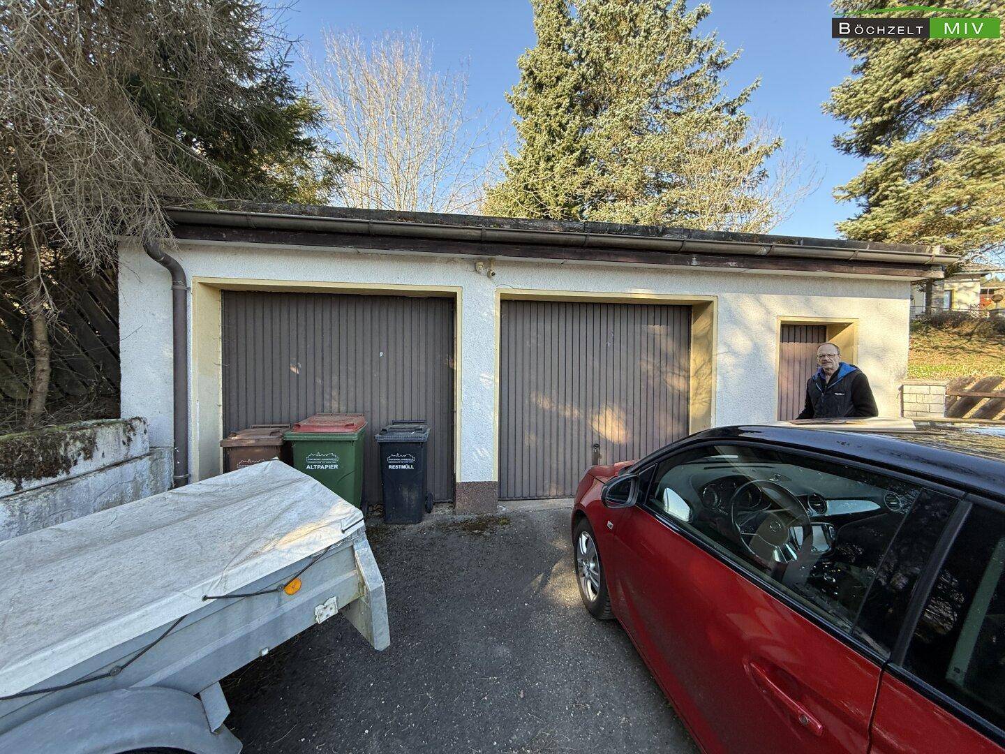Doppelgarage mit zwei Holztoren und einem zusätzlichen Eingang, daneben ein geparktes Auto.