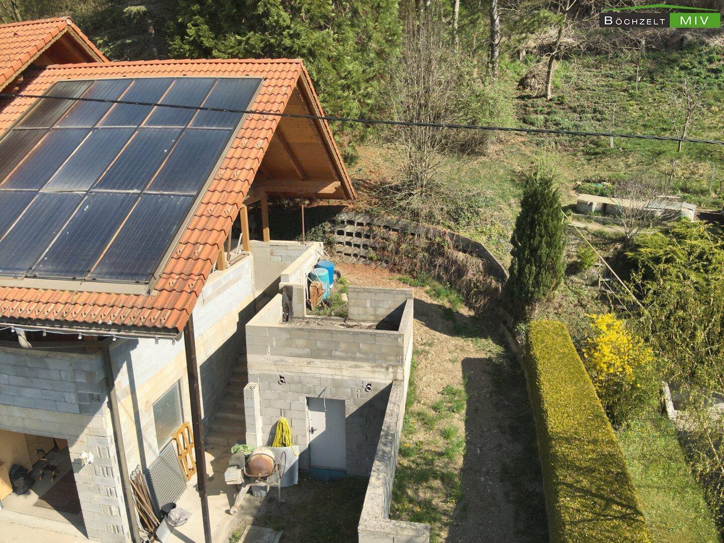 Nahaufnahme der Solaranlage auf dem Dach und eines unfertigen Anbaus mit Hecke.