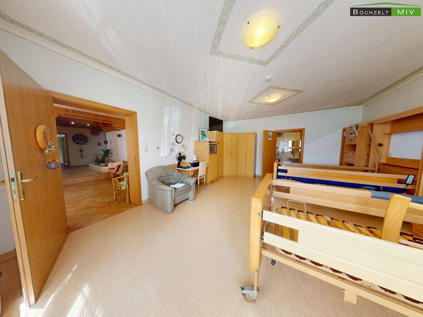 Schlafzimmer mit hellem Boden, Holzmöbeln und offenem Zugang zu einem weiteren Bereich.