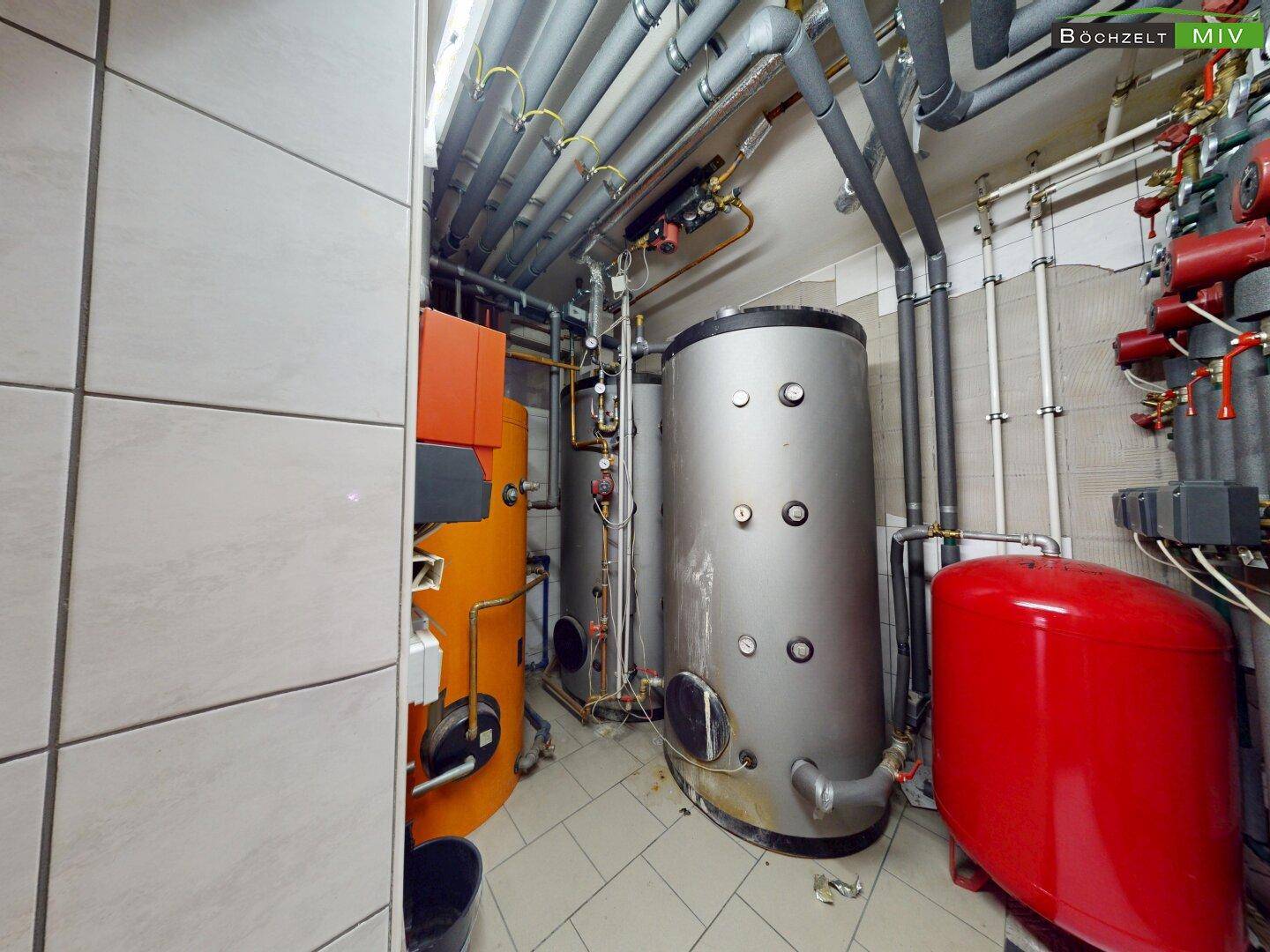 Technikraum mit großen Warmwasserspeichern, Rohrleitungen und Heizungsanlagen.
