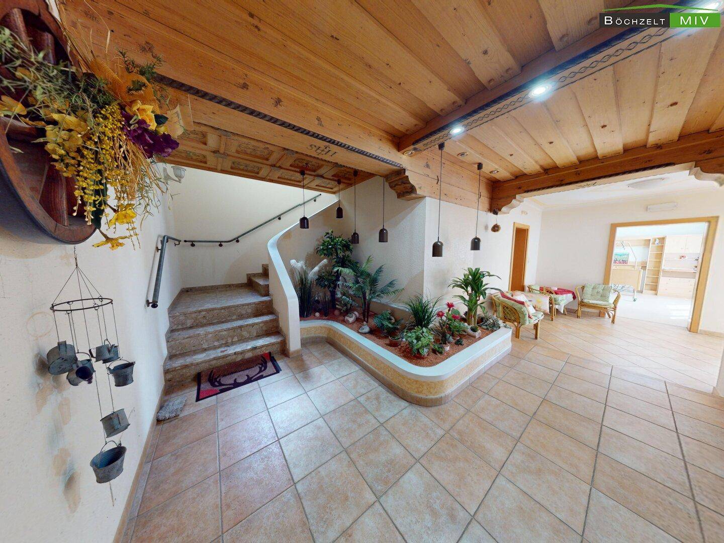 Geräumiger Eingangsbereich mit Holzdecke, gefliestem Boden und dekorativer Bepflanzung unter der Treppe.