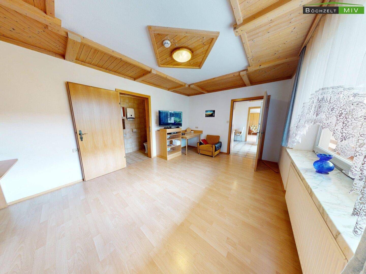 Helles Schlafzimmer mit Laminatboden, Holzdecke und Zugang zu weiteren Räumen.