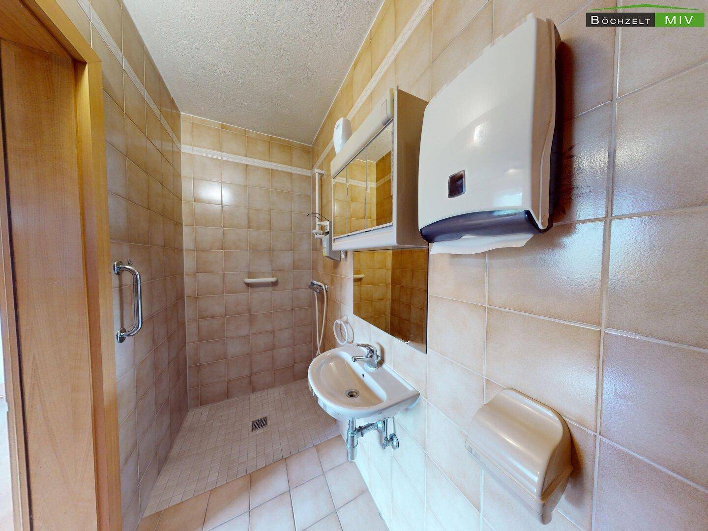 Badezimmer mit beigefarbenen Fliesen, einer ebenerdigen Dusche und einem einzelnen Waschbecken.