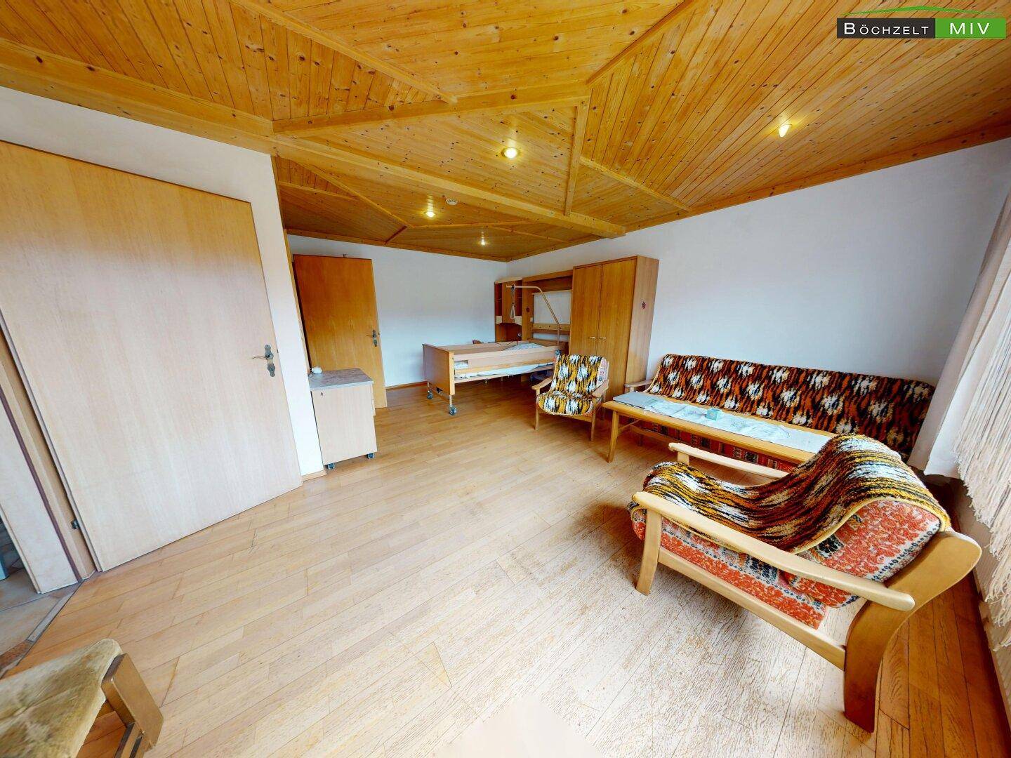 Geräumiges Zimmer mit Holzdecke, Laminatboden und einfacher Möblierung.
