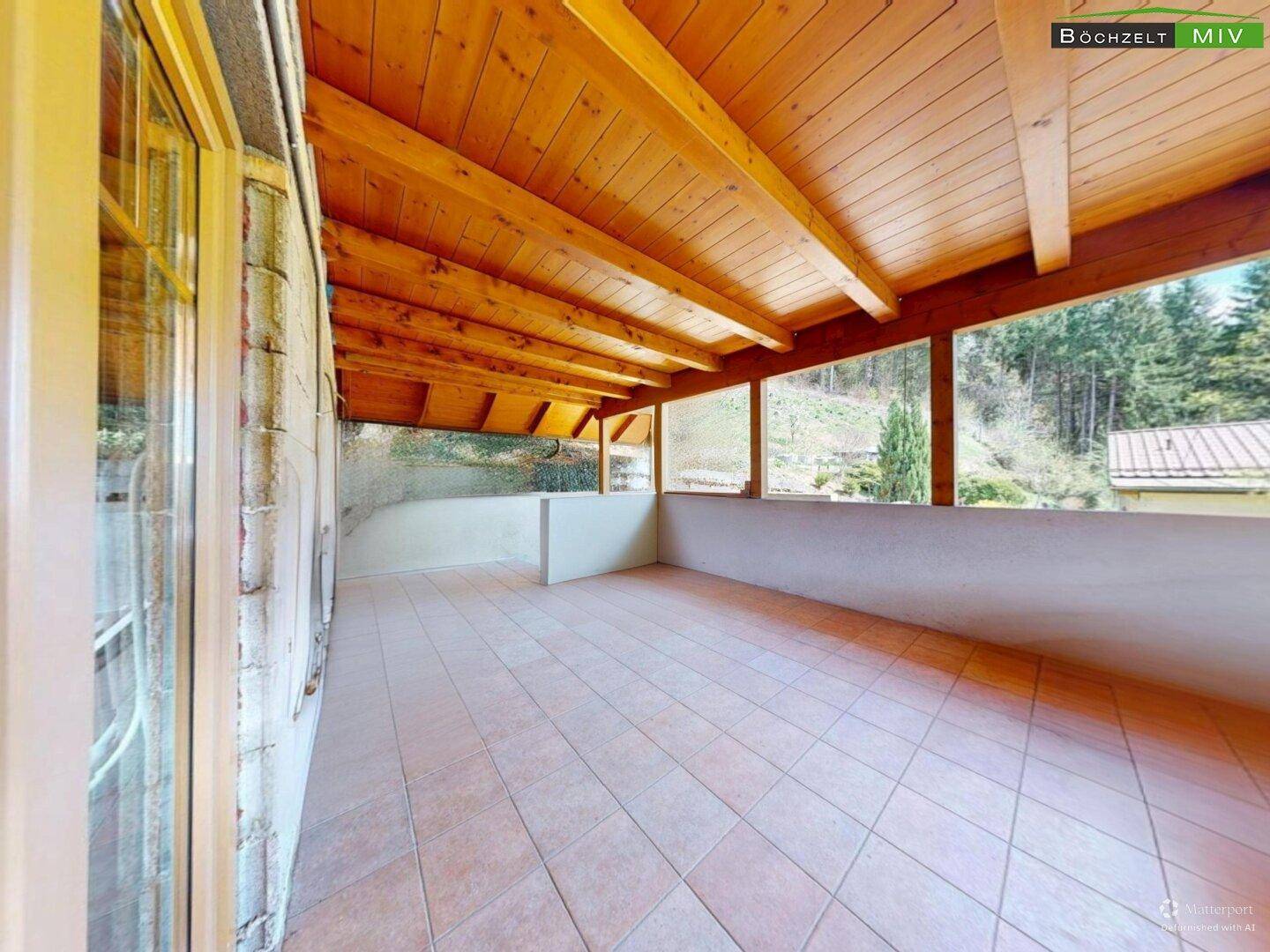 Überdachte Terrasse mit Fliesenboden und Holzdecke, bietet einen Blick ins Grüne.