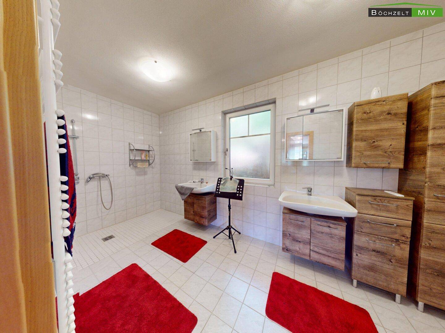 Modernes Badezimmer mit weißen Fliesen, zwei Waschbecken und ebenerdiger Dusche.