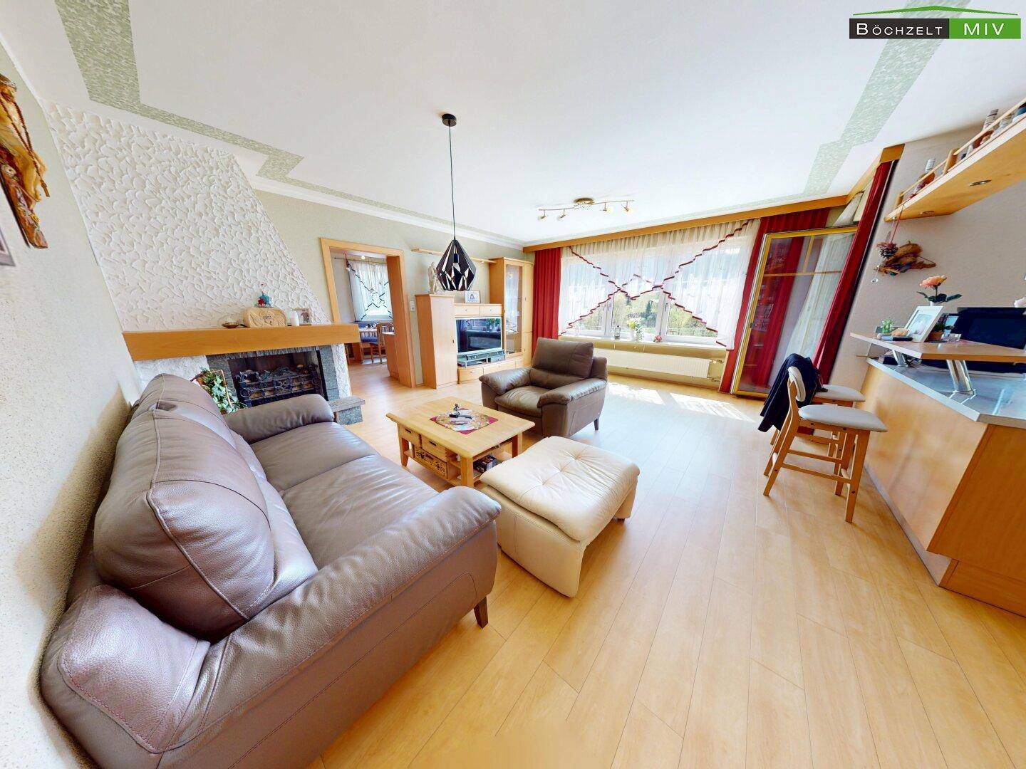 Helles Wohnzimmer mit Kamin, Ledersofa, Holzboden und großen Fenstern.