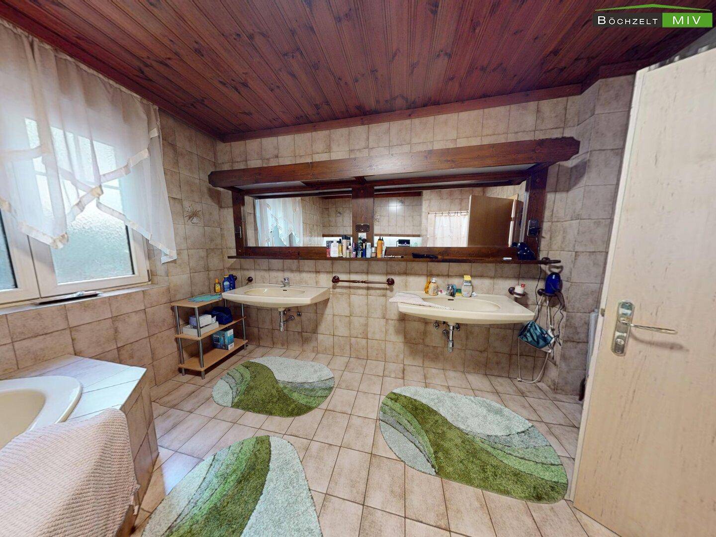 Badezimmer mit Doppelwaschbecken, großem Spiegel und gefliesten Wänden unter einer Holzdecke.