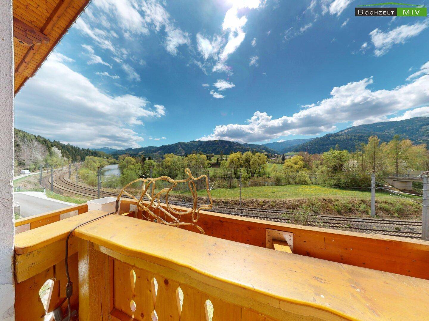 Balkon mit traditionellem Holzgeländer und weitem Blick auf die umliegende Landschaft und Berge.