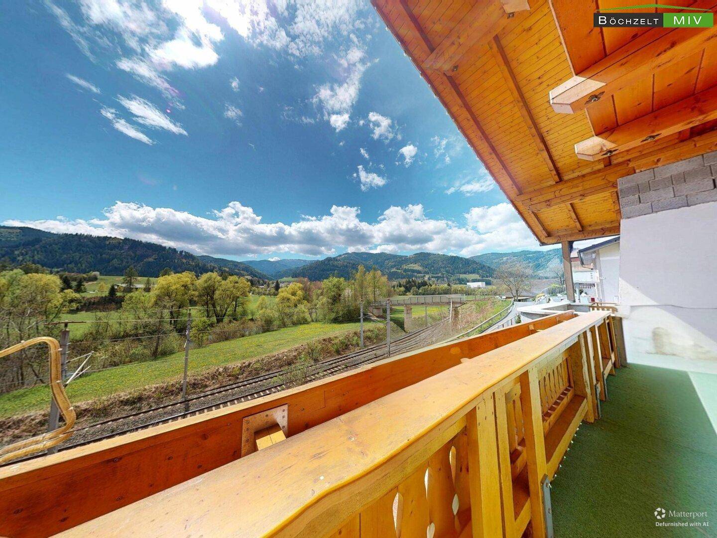 Langer Balkon mit Kunstrasen und Panoramablick auf die grüne Landschaft und die Berge.