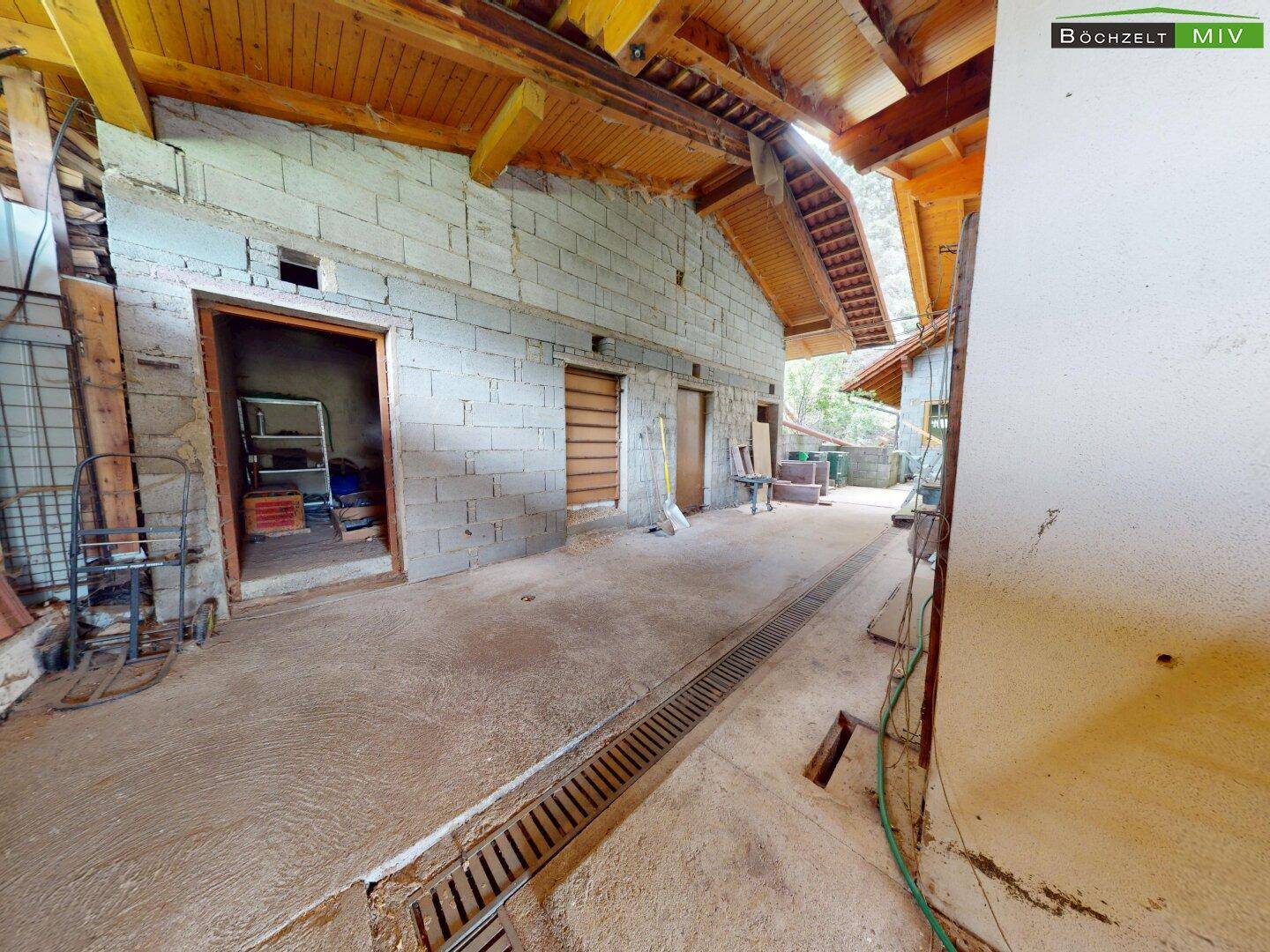 Geräumiger Garagenbereich mit Betonboden und sichtbaren Holzdeckenbalken, ideal als Werkstatt.