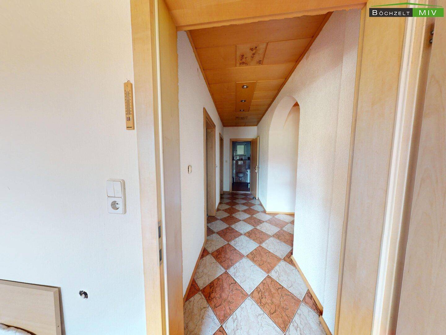 Flur mit gemustertem Fliesenboden und Holzdecke, der zu weiteren Räumen führt.
