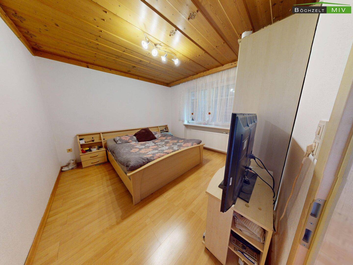 Schlafzimmer mit Holzboden, Doppelbett und Holzdecke, hell und funktional eingerichtet.