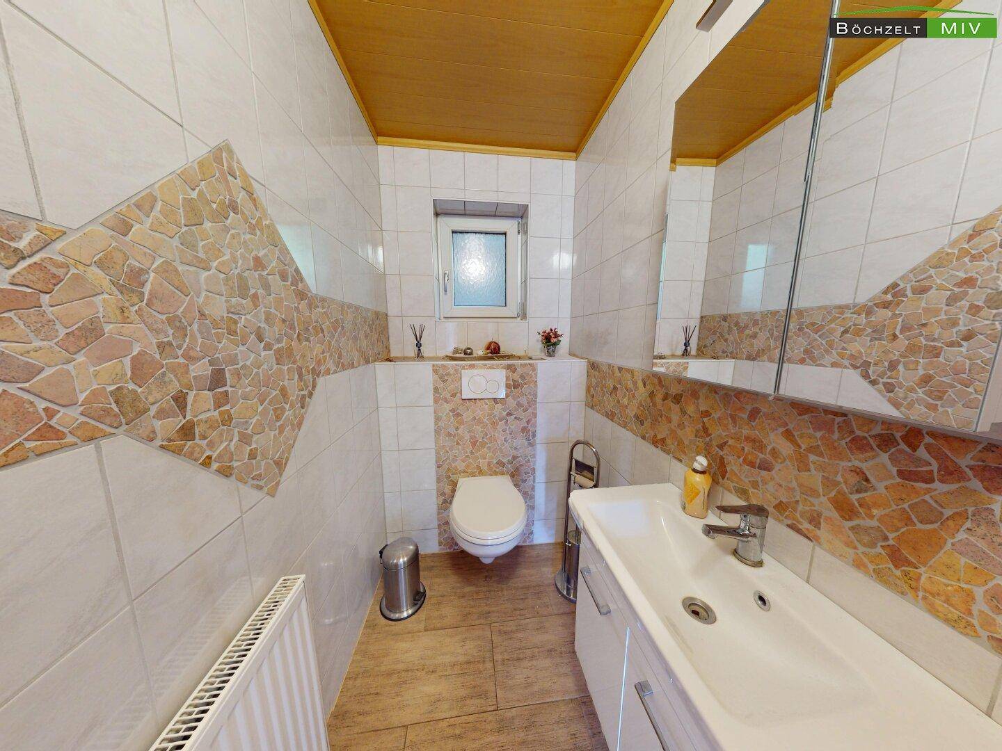 Modern gefliestes Gäste-WC mit Waschbecken, Spiegel und dekorativen Steinakzenten.