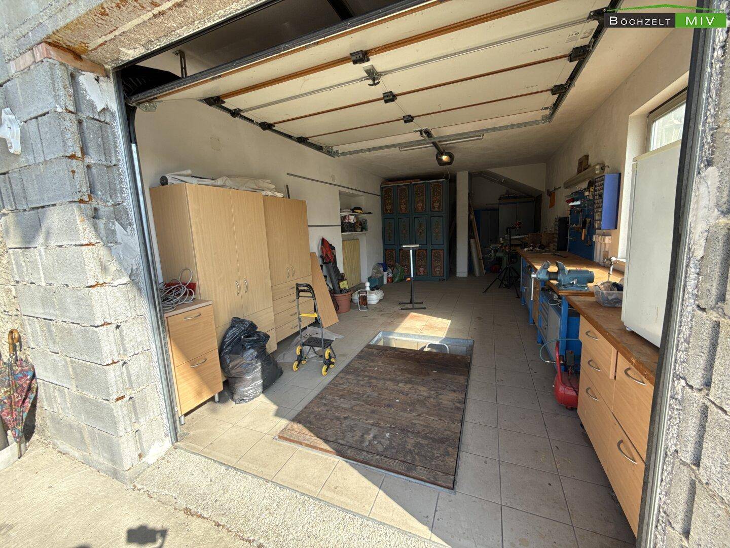 Geräumige Garage mit Werkstattbereich, Fliesenboden und viel Stauraum für Fahrzeuge und Geräte.