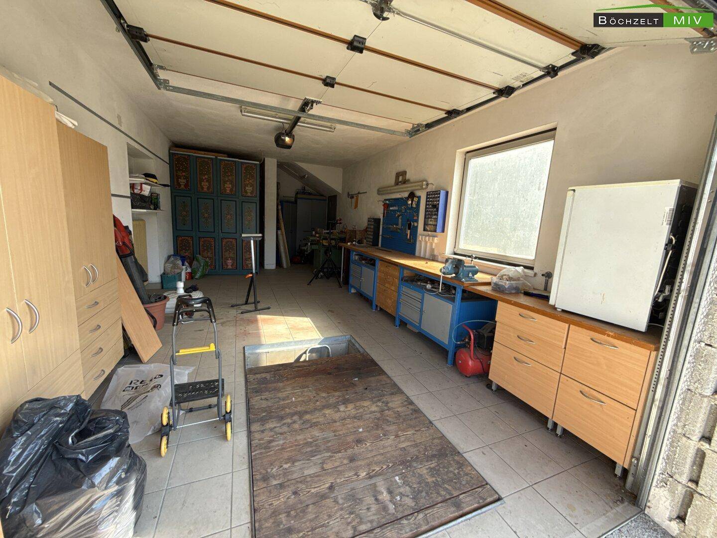 Große Garage mit Werkbank, Fliesenboden und Tageslicht durch ein Fenster.