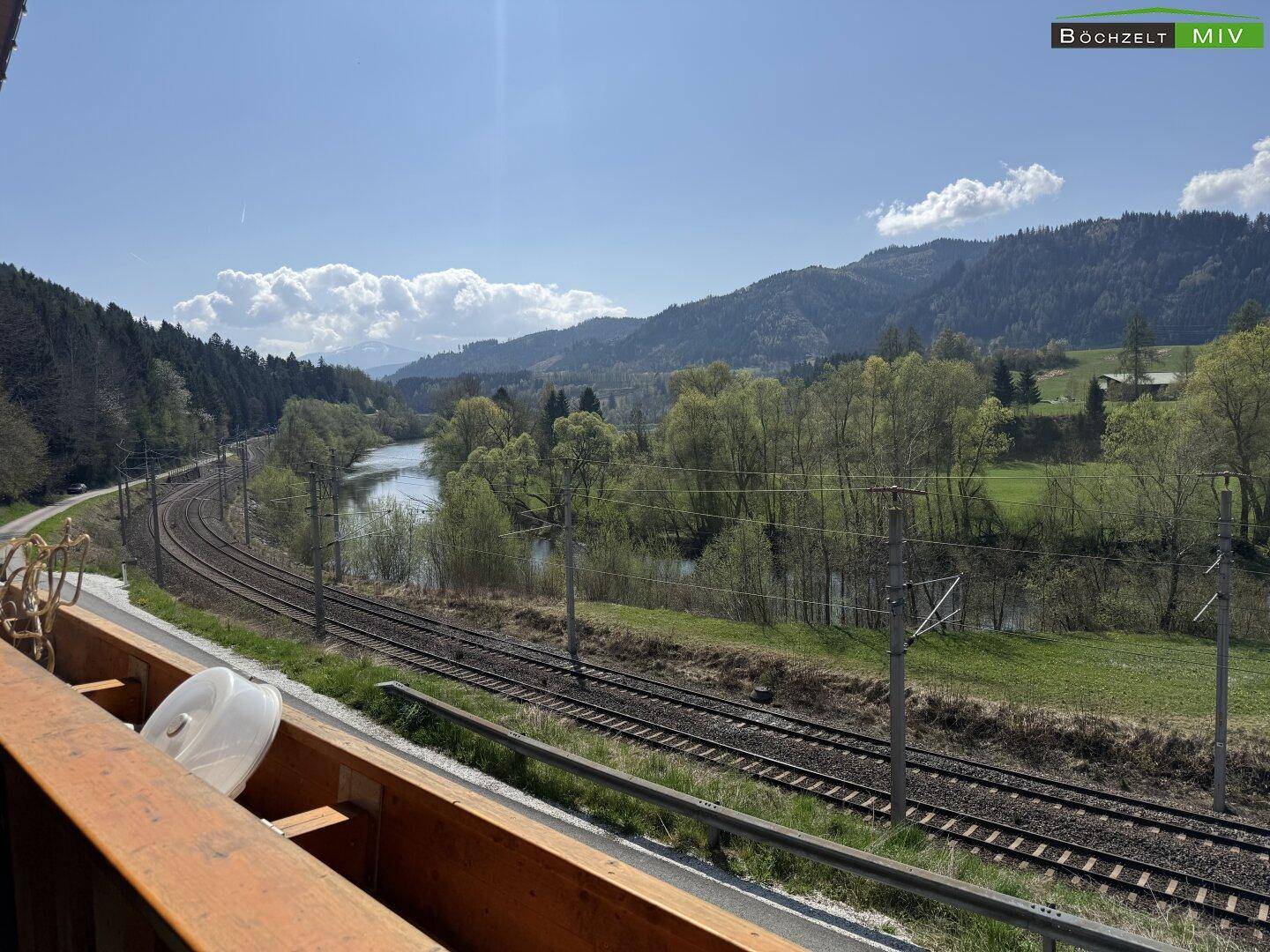 Balkon mit weitem Blick auf die Bahngleise, den Fluss und die umliegende Berglandschaft.