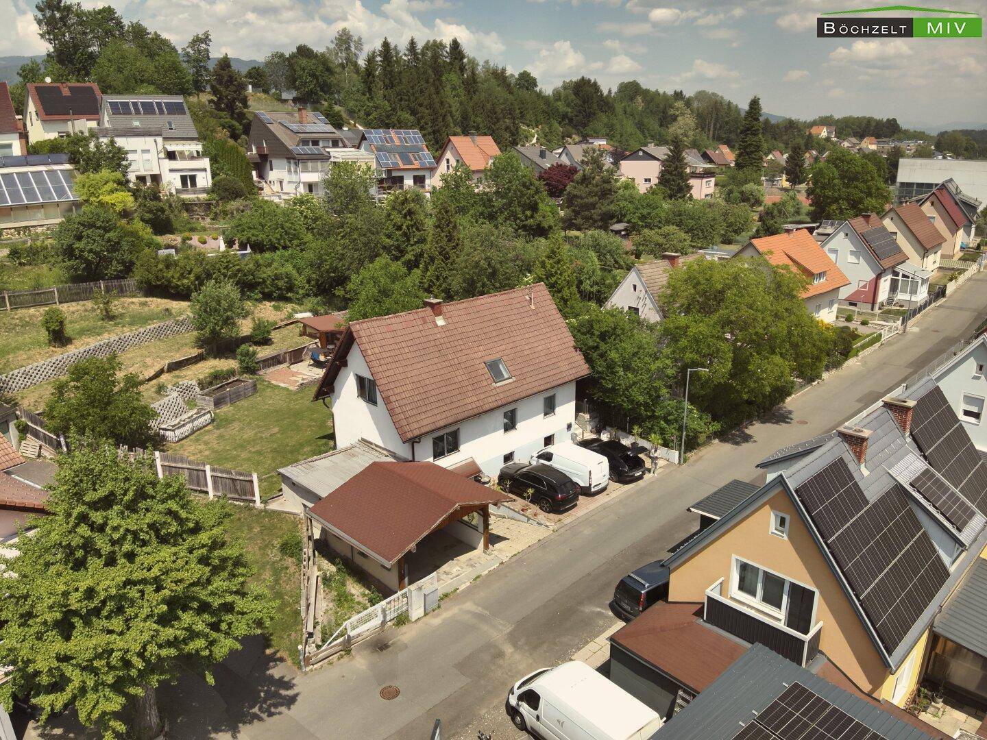 Weitläufige Luftaufnahme eines Wohnhauses mit umliegenden Gärten und Dächern mit Solaranlagen.