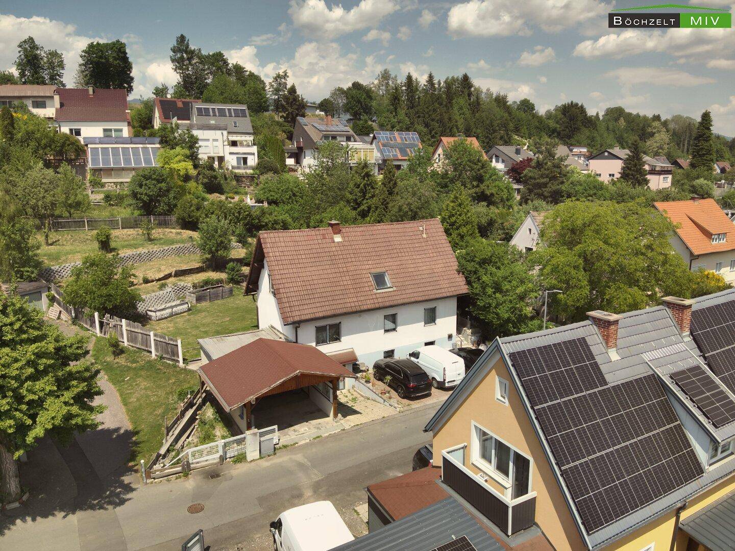 Luftbild des Wohnhauses mit Carport, umgeben von grünen Bäumen und anderen Häusern mit Solaranlagen.