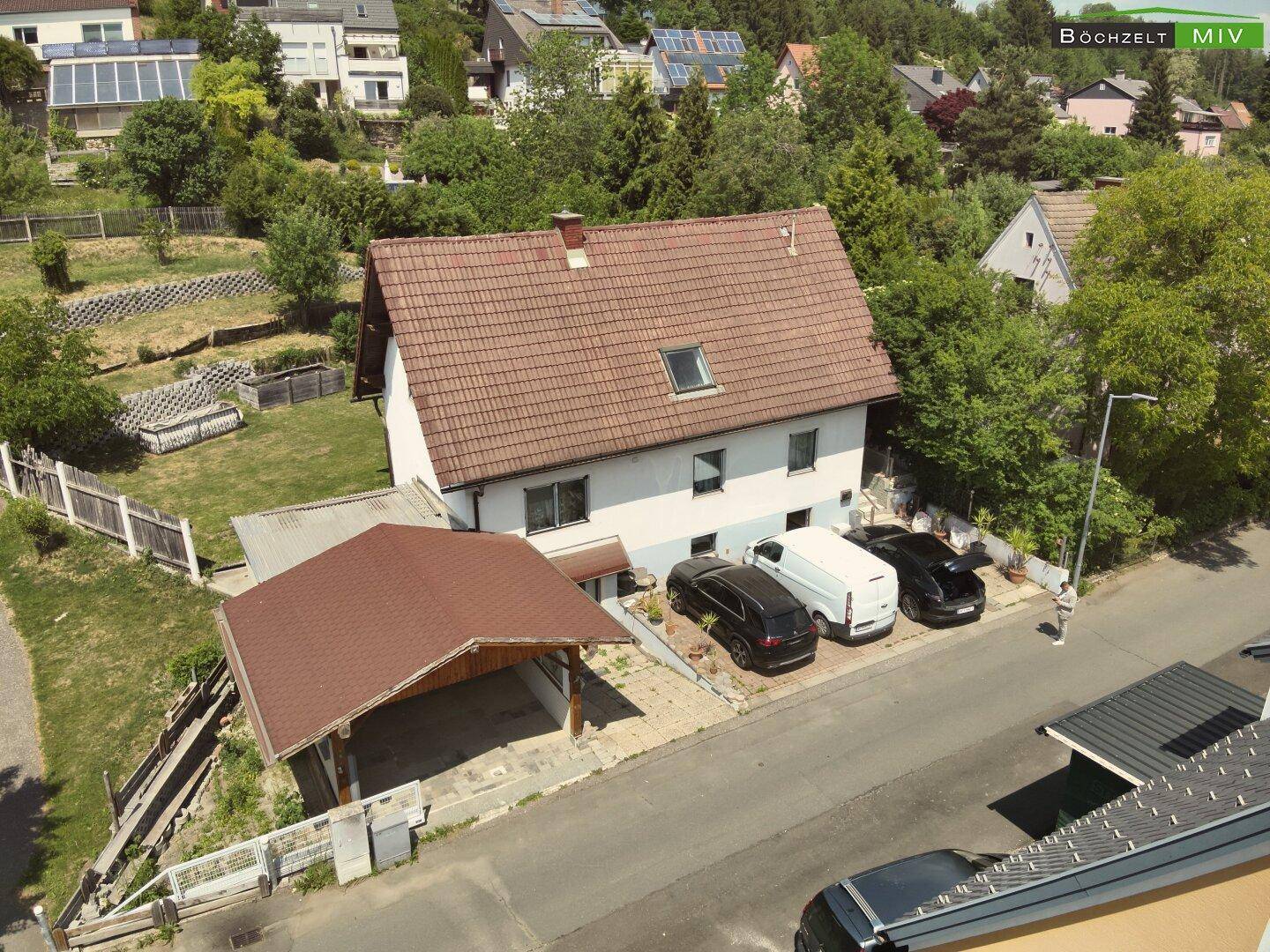 Drohnenansicht des Einfamilienhauses mit Carport und Garten, eingebettet in eine grüne Umgebung.