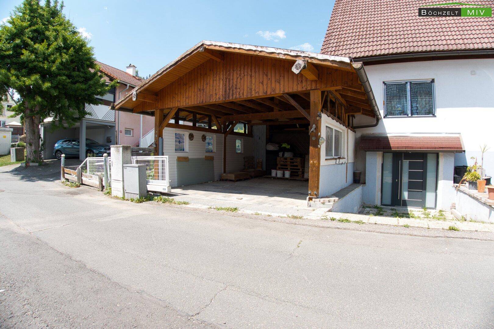 Eingangsbereich des Hauses mit modernem Carport aus Holz und gepflastertem Vorplatz.