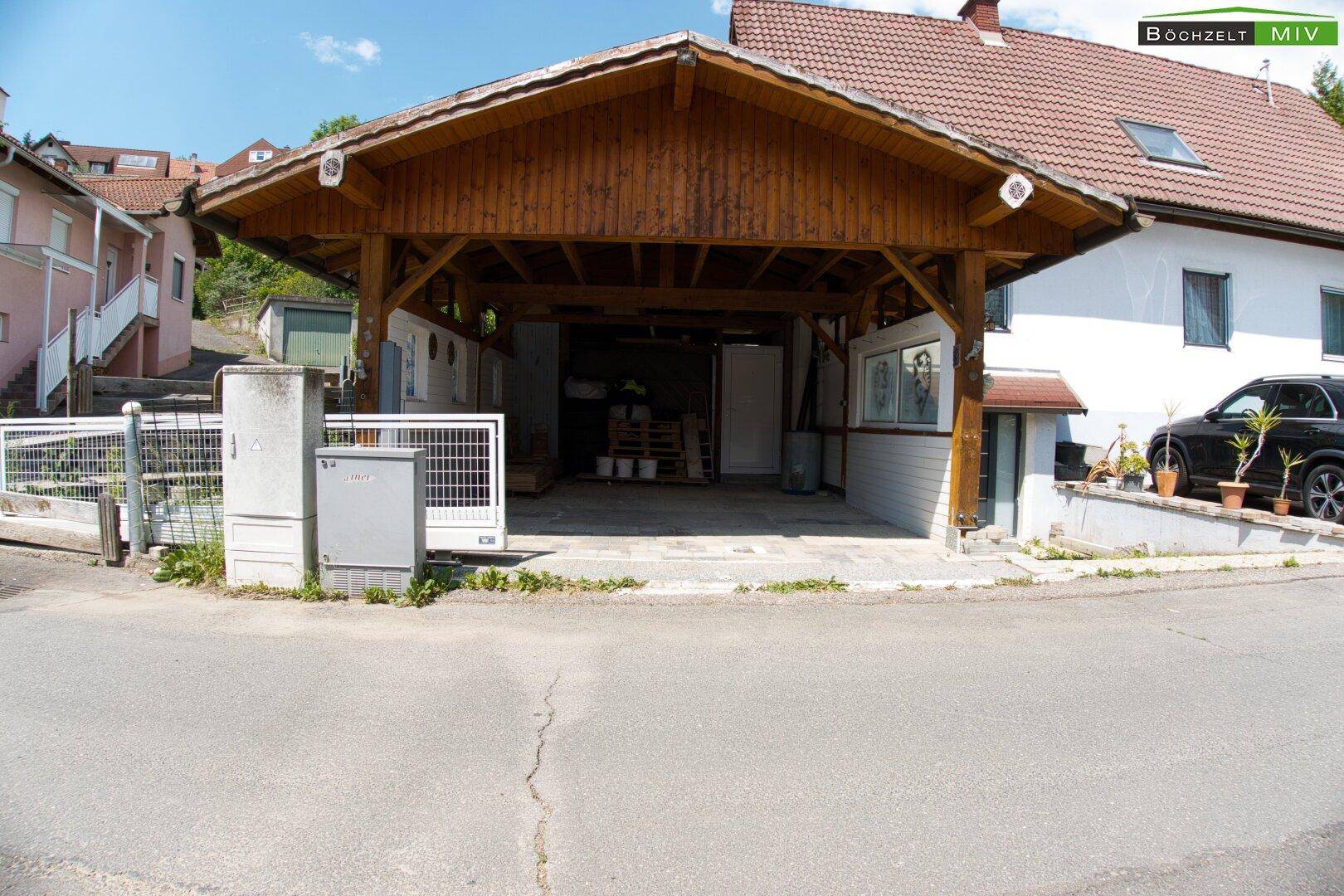 Ansicht des Carports mit Holzbalkenkonstruktion und dem Hauseingangsbereich von der Straße aus.