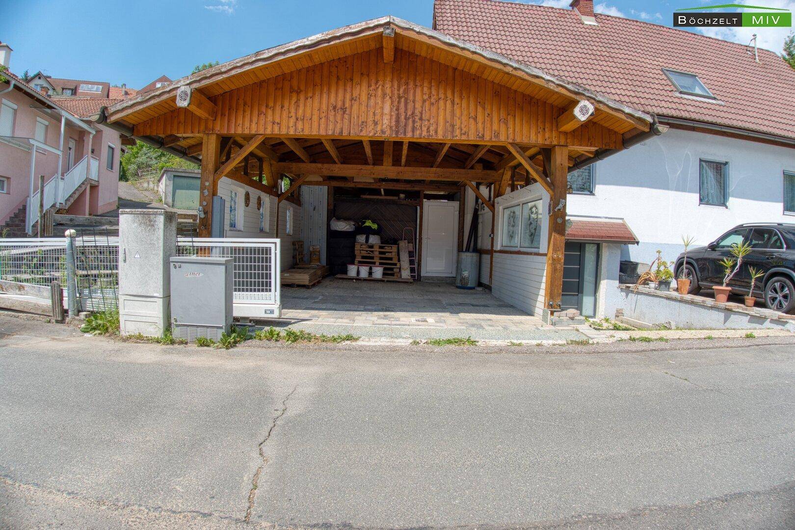Blick auf das Wohnhaus mit großem Holzcarport und gepflastertem Vorplatz für Fahrzeuge.